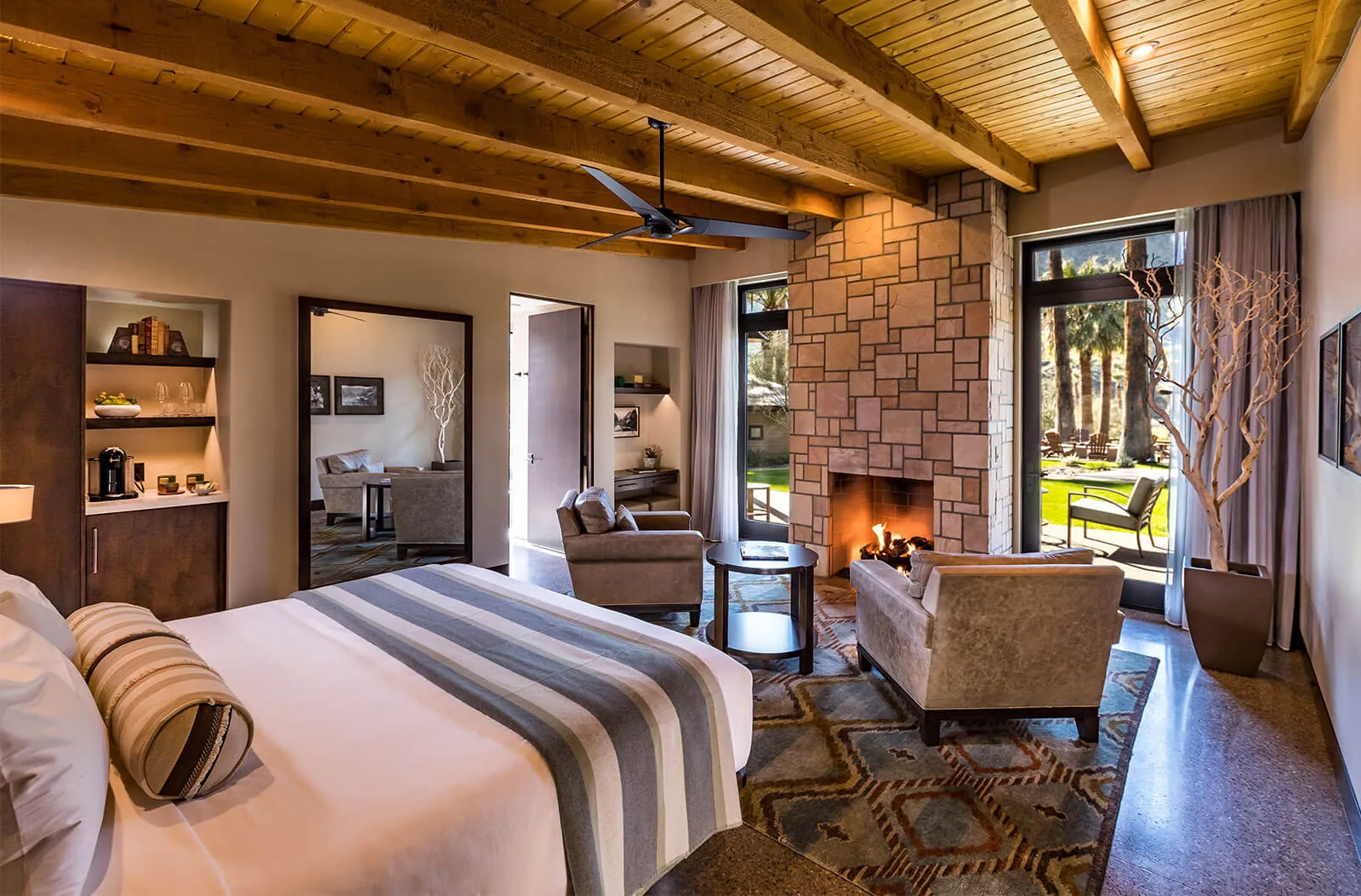 Cozy bungalow with wooden ceiling, fireplace, and outdoor view through large glass doors.