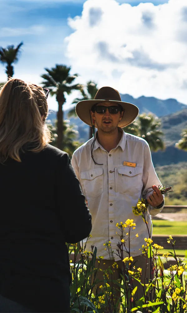 A farm tour guide and a guest in a sunny garden at Castle Hot Springs resort.