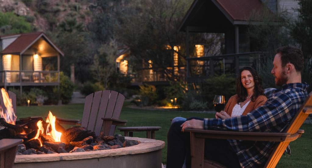 During a romantic getaway in Arizona, a couple sip wine while sitting in chairs by an outdoor firepit.