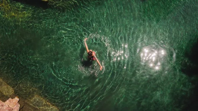 A person swimming in a hot spring, creating ripples around them, viewed from above.