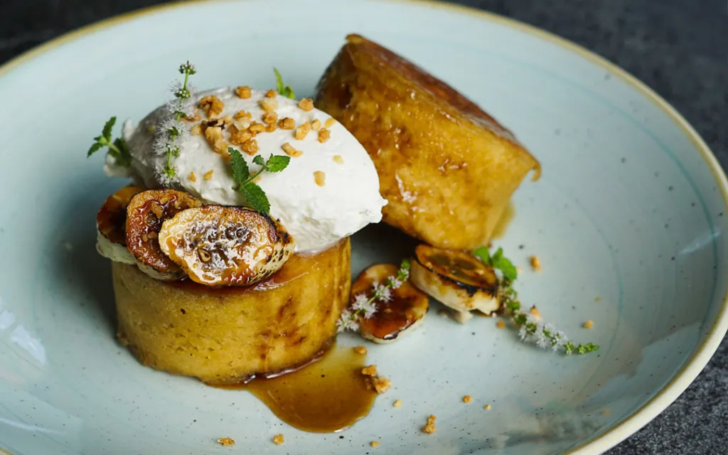 Gourmet dessert with caramelized banana, vanilla ice cream, nuts, and edible flowers on a plate.