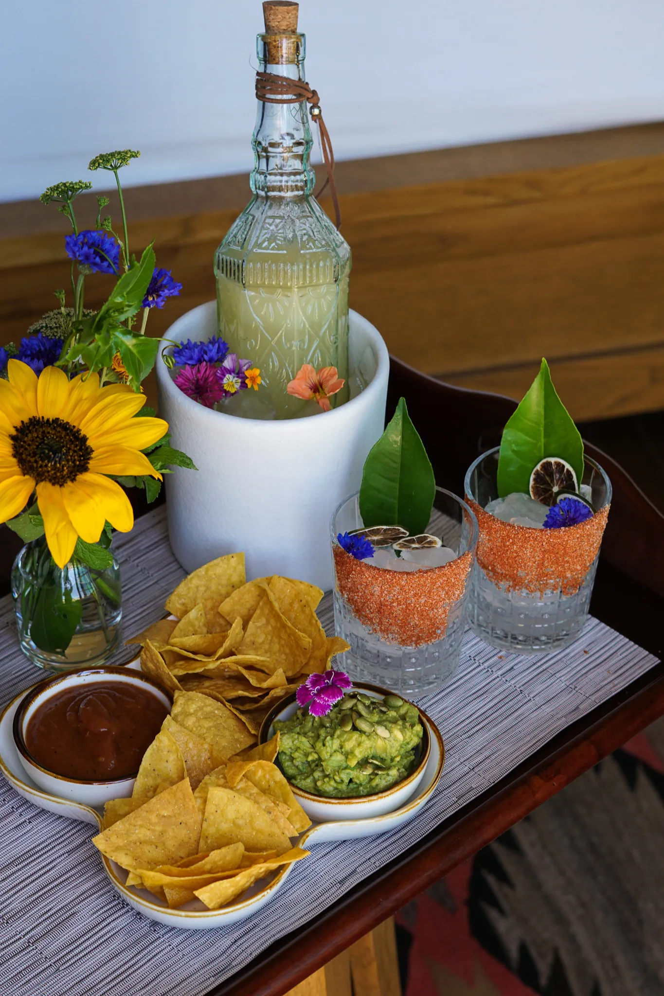 Table with chips, guacamole, salsa, margarita glasses, and a tequila bottle on ice.