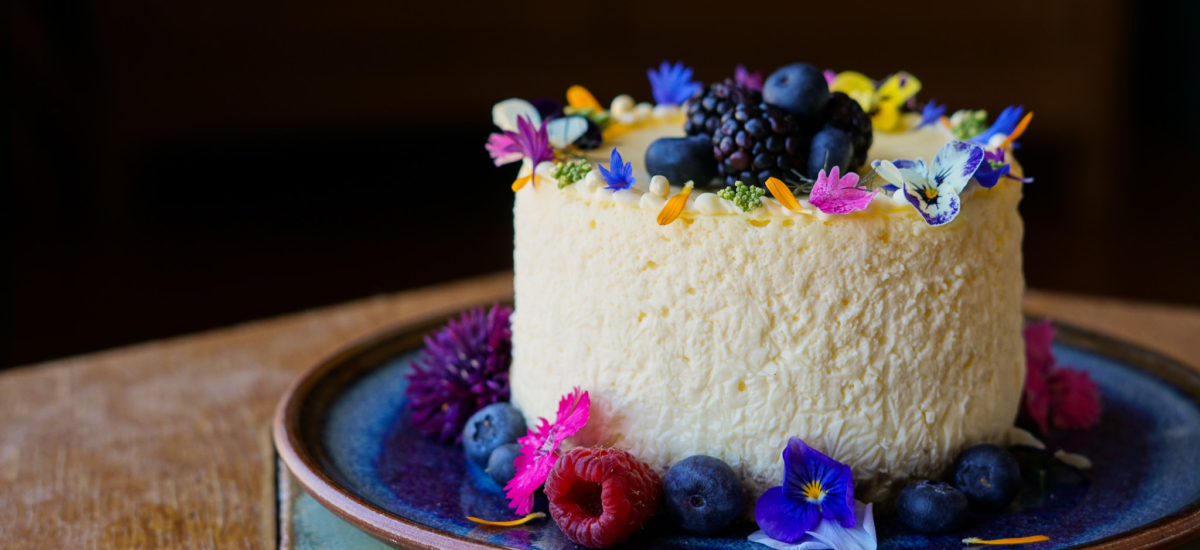 White layered artisan cake topped with blackberries, raspberries, blueberries, and edible flowers.