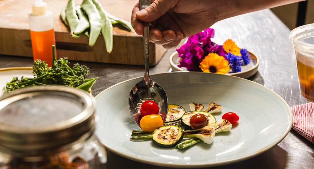 Spooning fresh vegetables onto a plate at Harvest farm-to-table dining