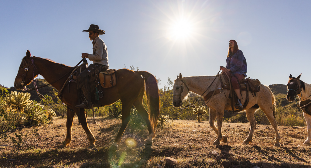 Two people on a guided horseback ride at Castle Hot Springs with the sun in the sky