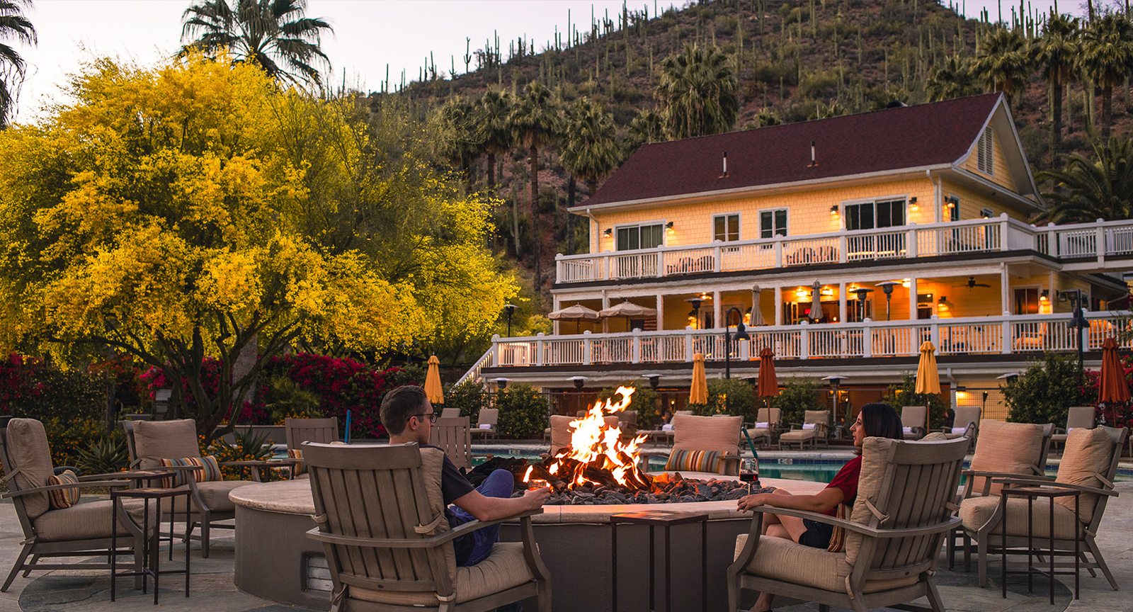 A couple sitting around a firepit with a yellow lodge in the background