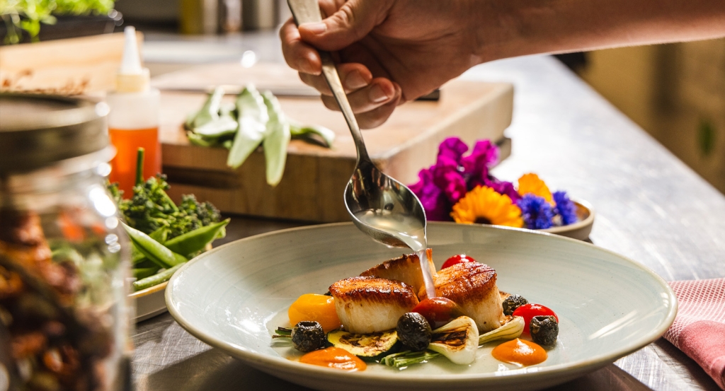 Ladling sauce onto a gourmet farm to table dish at Harvest Restaurant